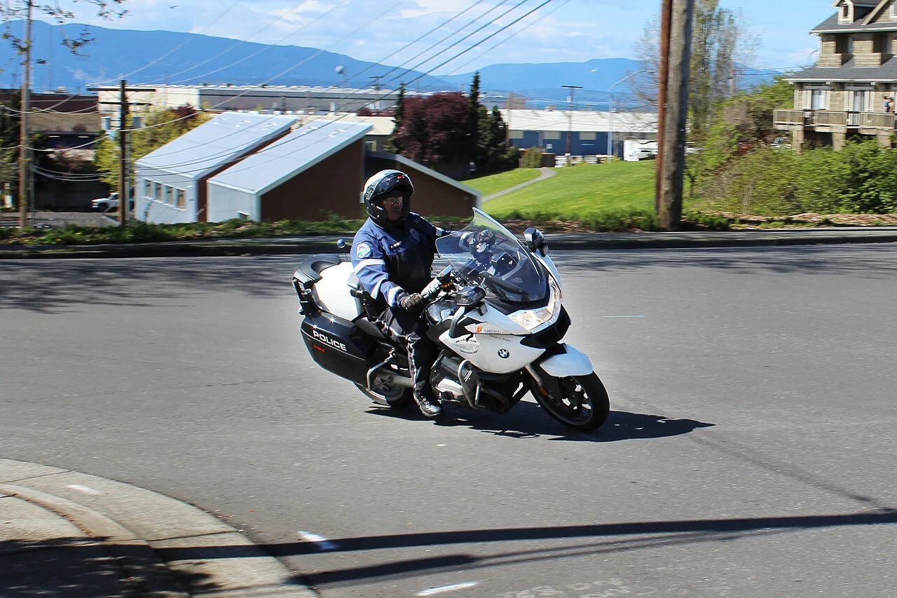 A traffic-enforcement officer rides a white BMW police motorcycle marked 'POLICE' on a road.