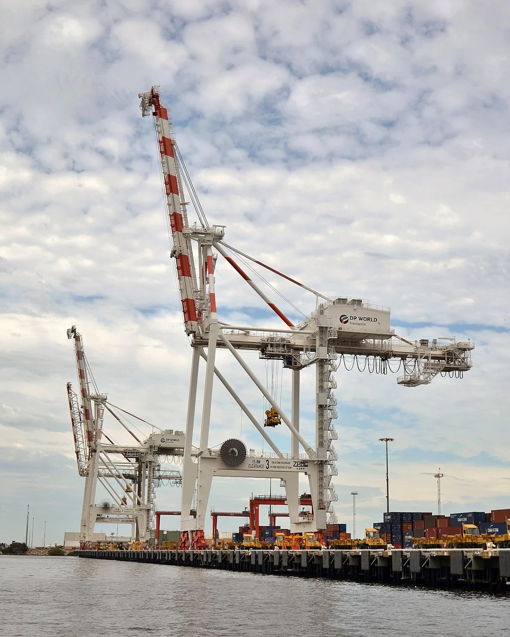 Large container cranes stand on a quay beside stacked shipping containers.
