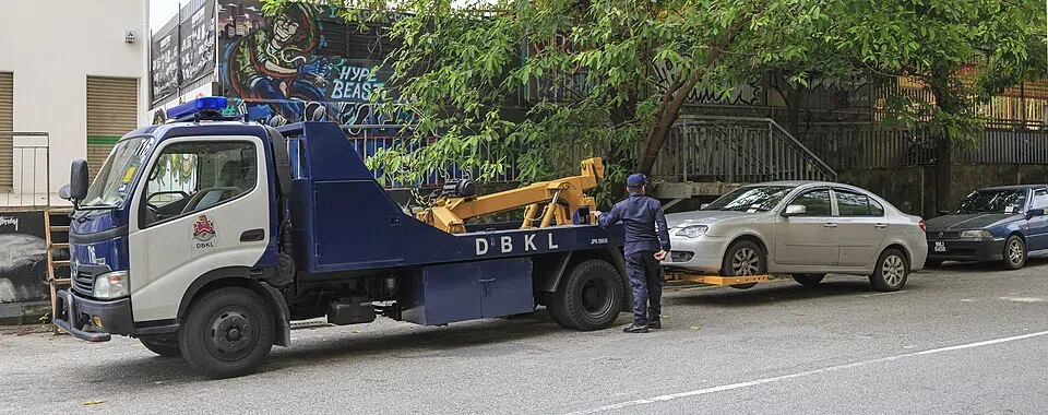 A small blue-and-white recovery truck is parked beside the road.