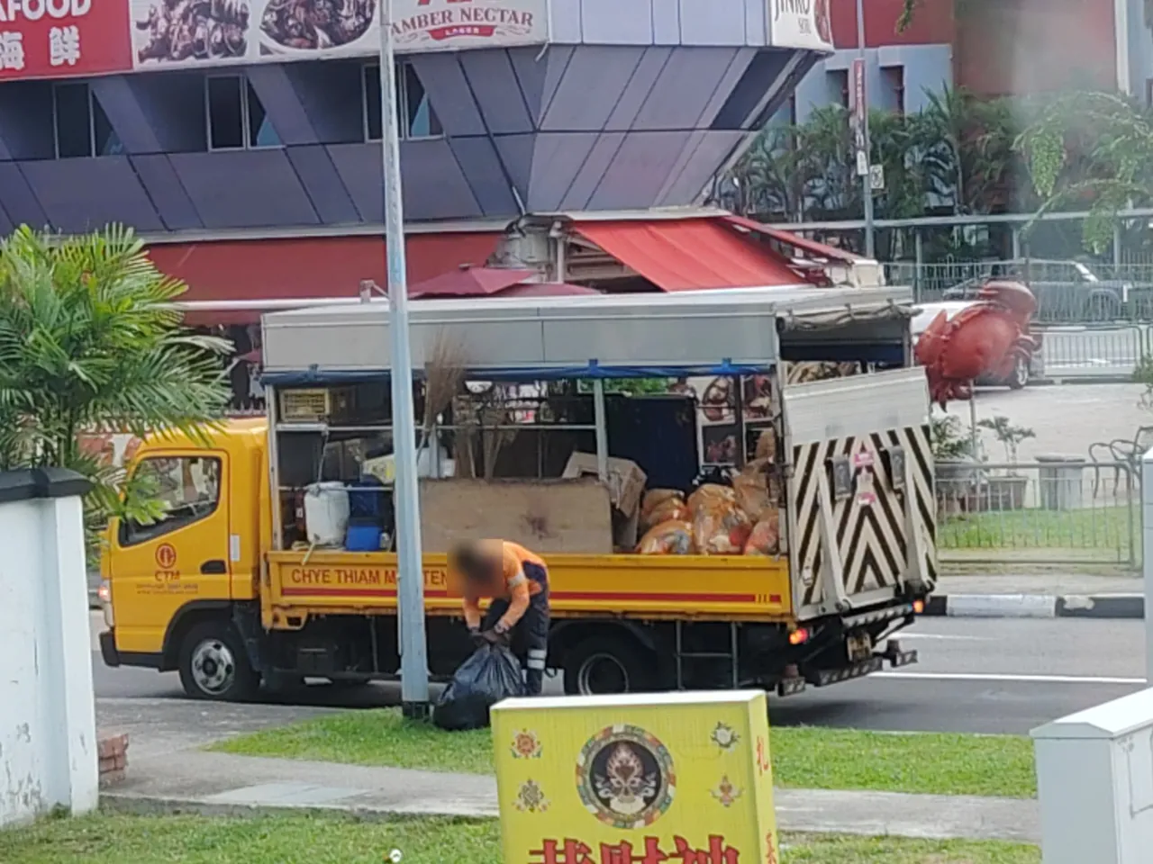 Refuse truck — a yellow lorry being loaded with bags of rubbish, photographed in Singapore.
