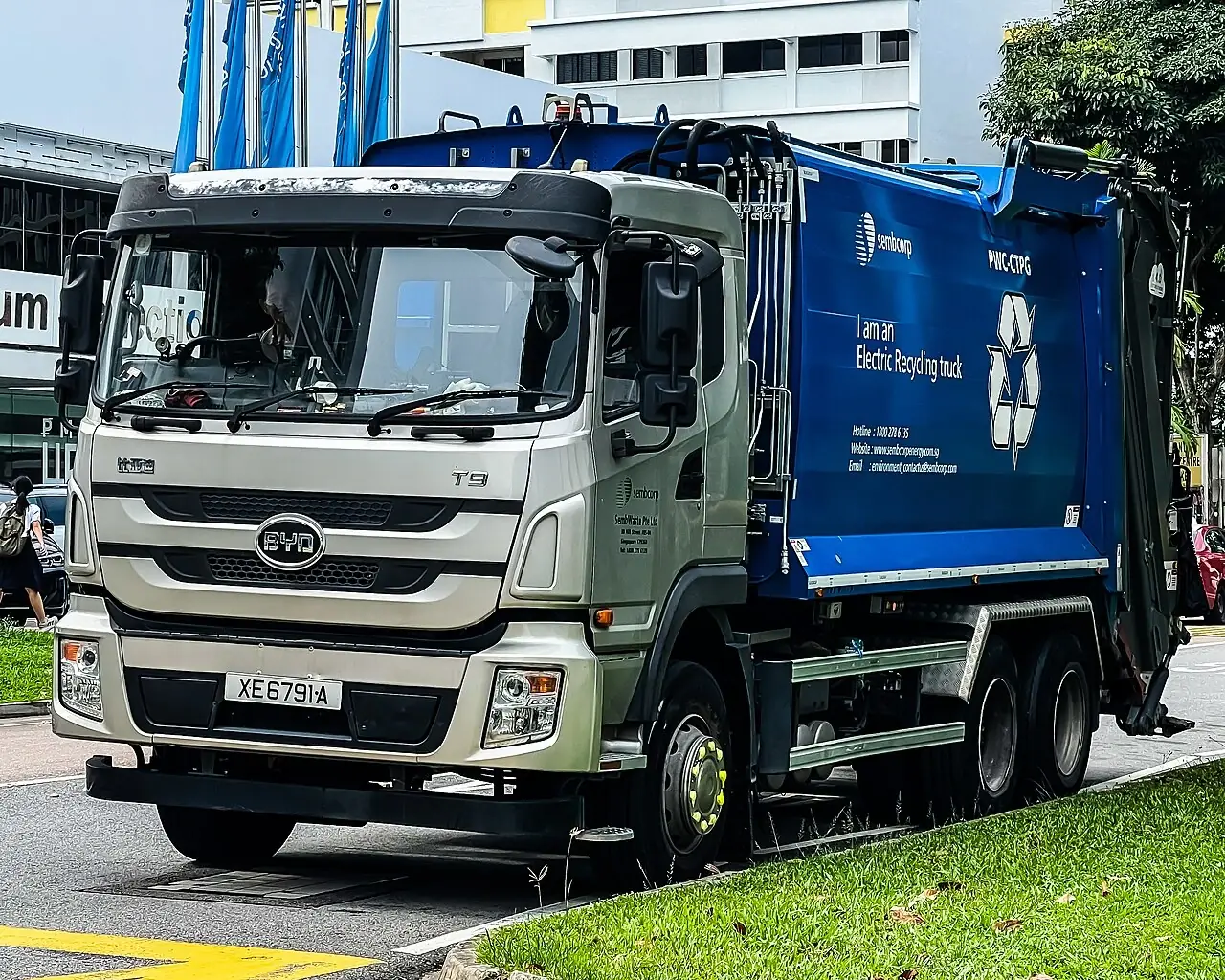 A grey refuse truck has a large blue collection body behind the cab.