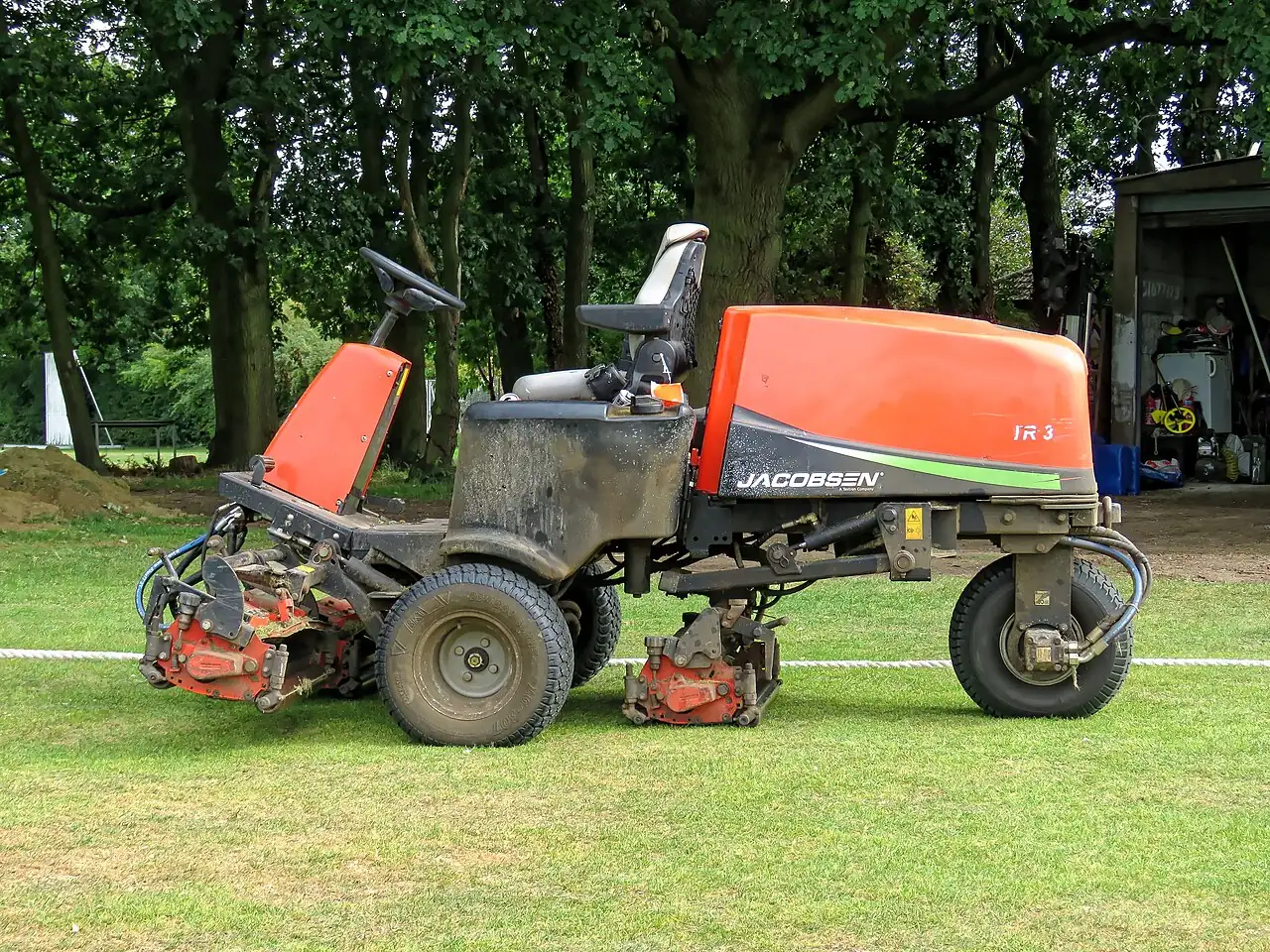 A ride-on lawn mower has several cutting units near the grass.