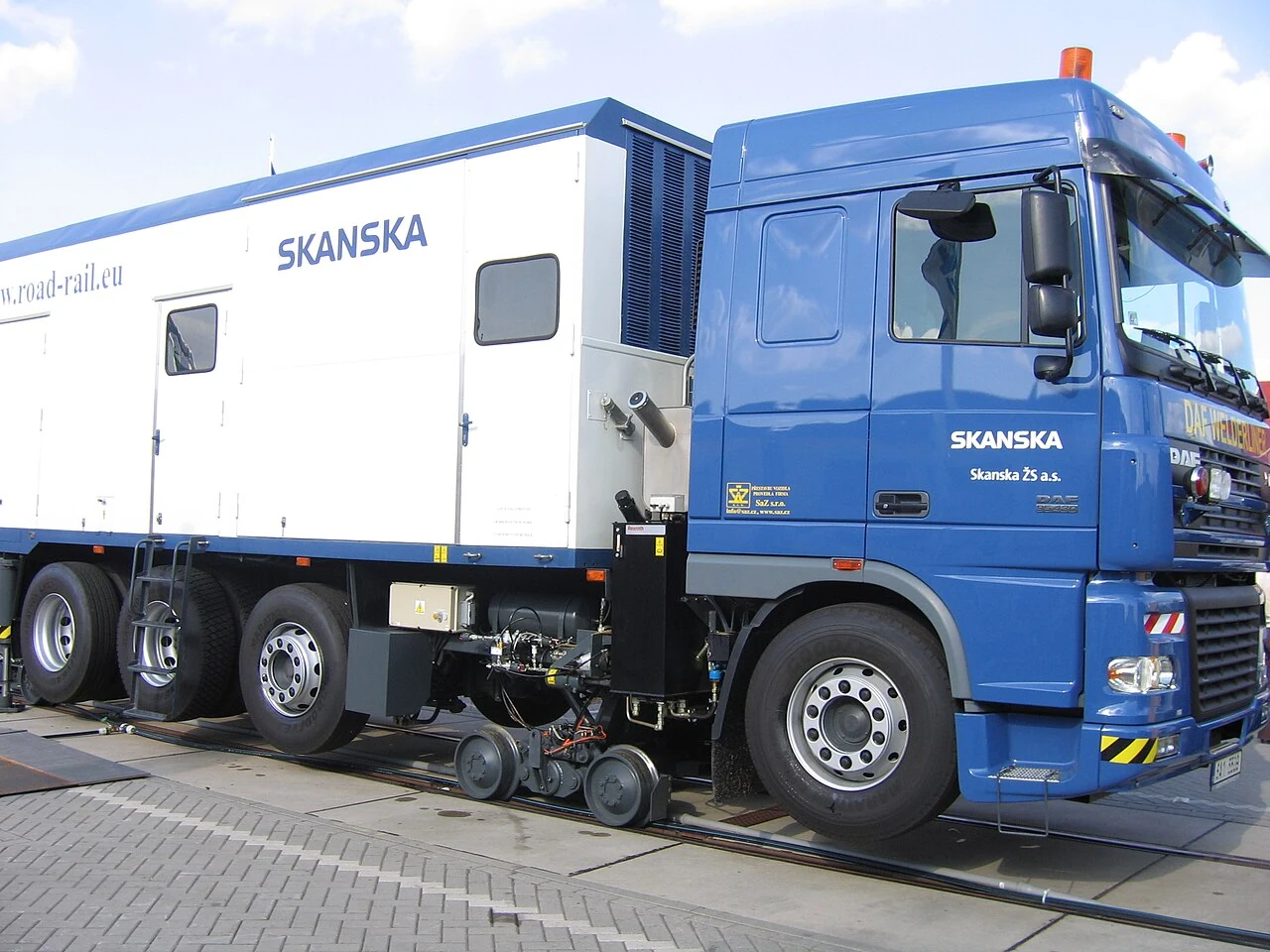 A blue-and-white truck has small rail wheels lowered beneath its large road tyres.