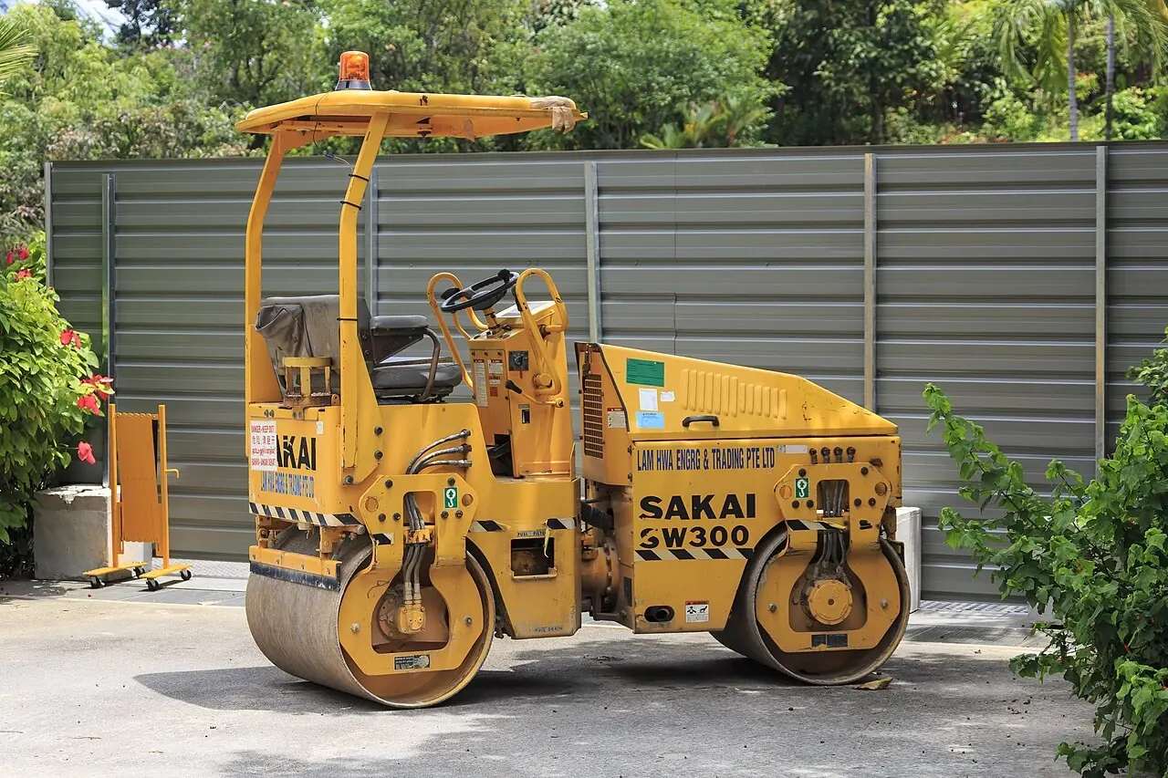 A small yellow road roller has two smooth metal drums and an open driver's seat.