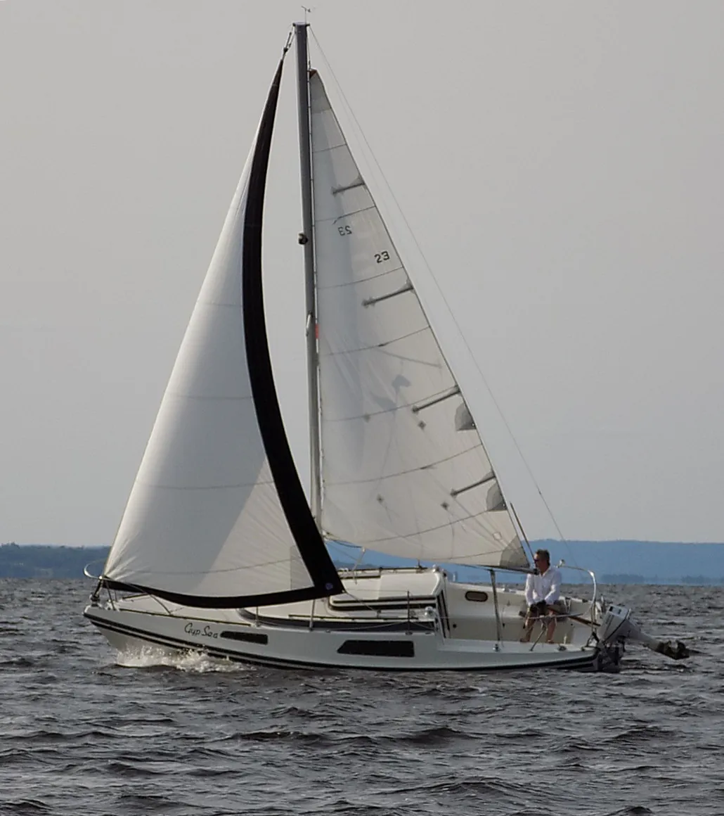 A white sailing boat has two tall sails above its narrow hull.