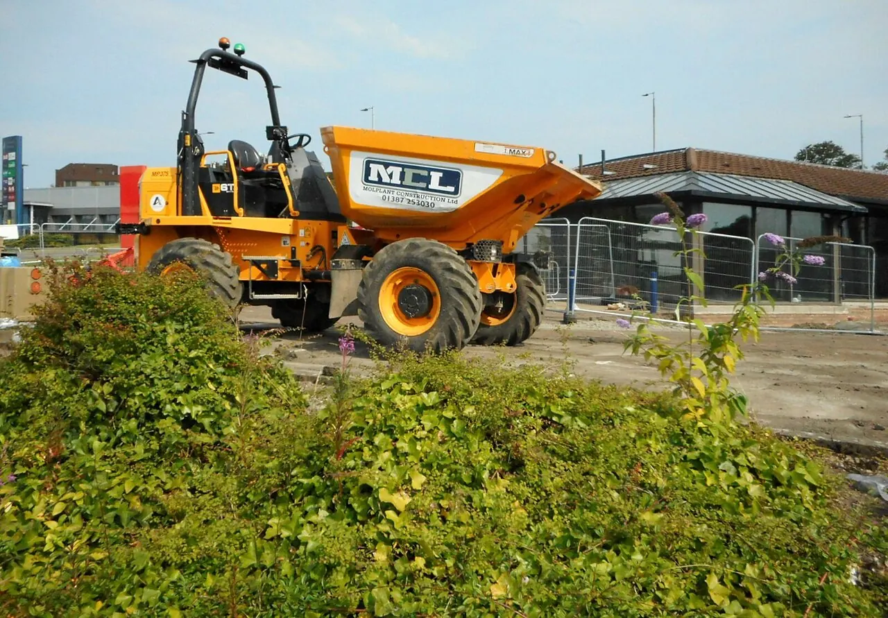 A yellow site dumper has a large tipping skip in front of its driver seat.