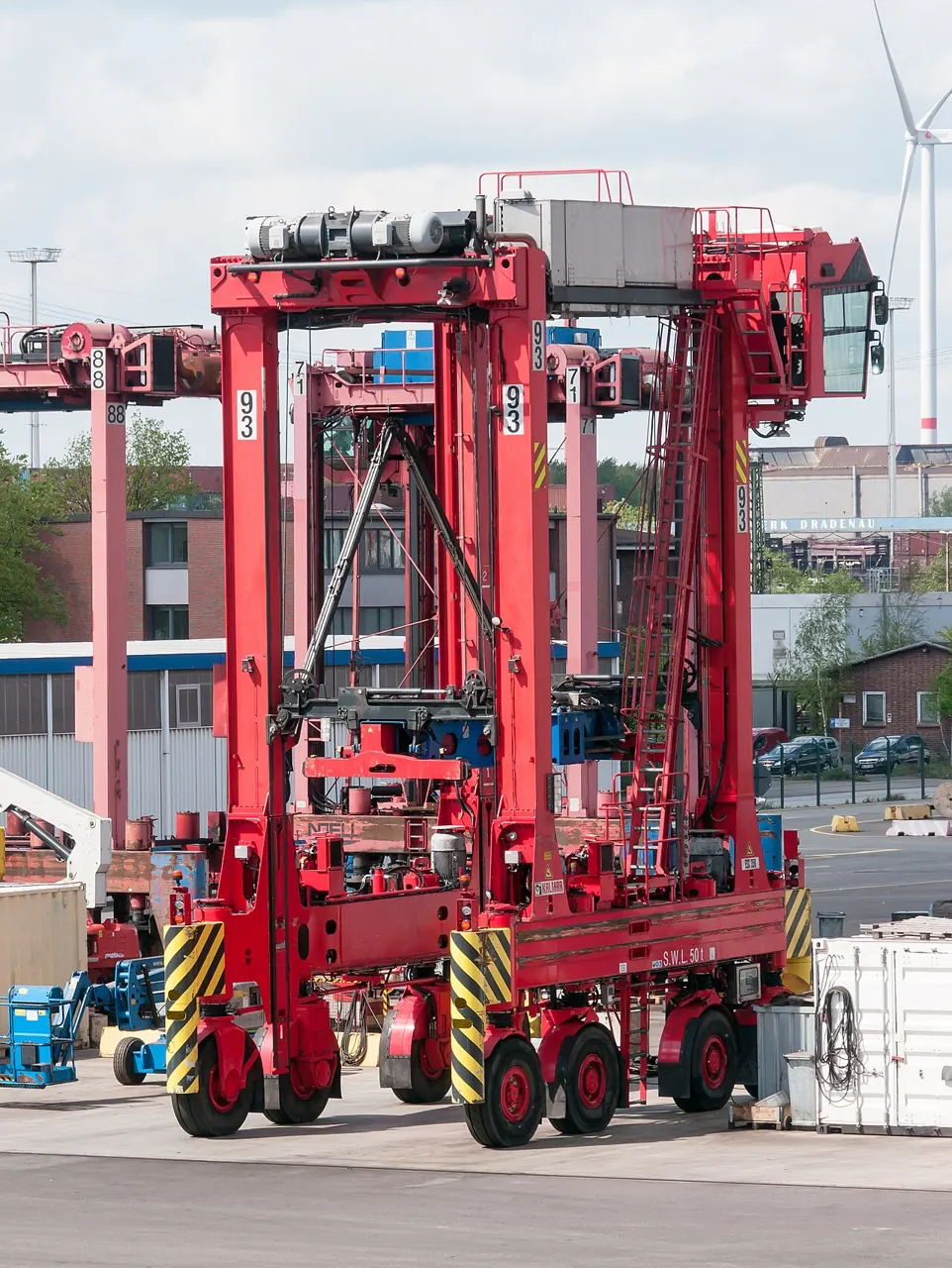 A tall red straddle carrier has wheels along both sides.