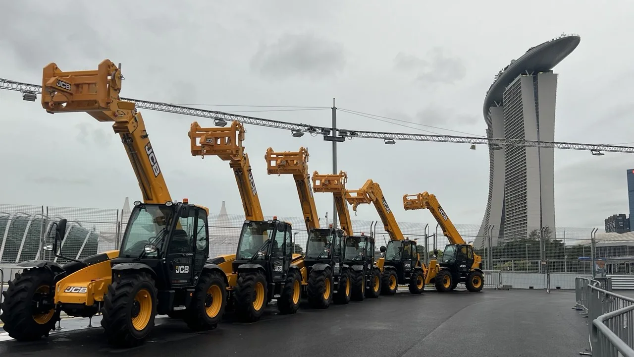 Yellow telehandlers stand in a row with their booms raised.