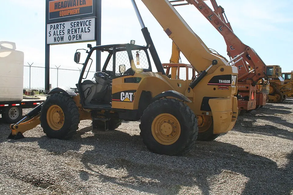A yellow telehandler has four large tyres and a raised lifting arm.