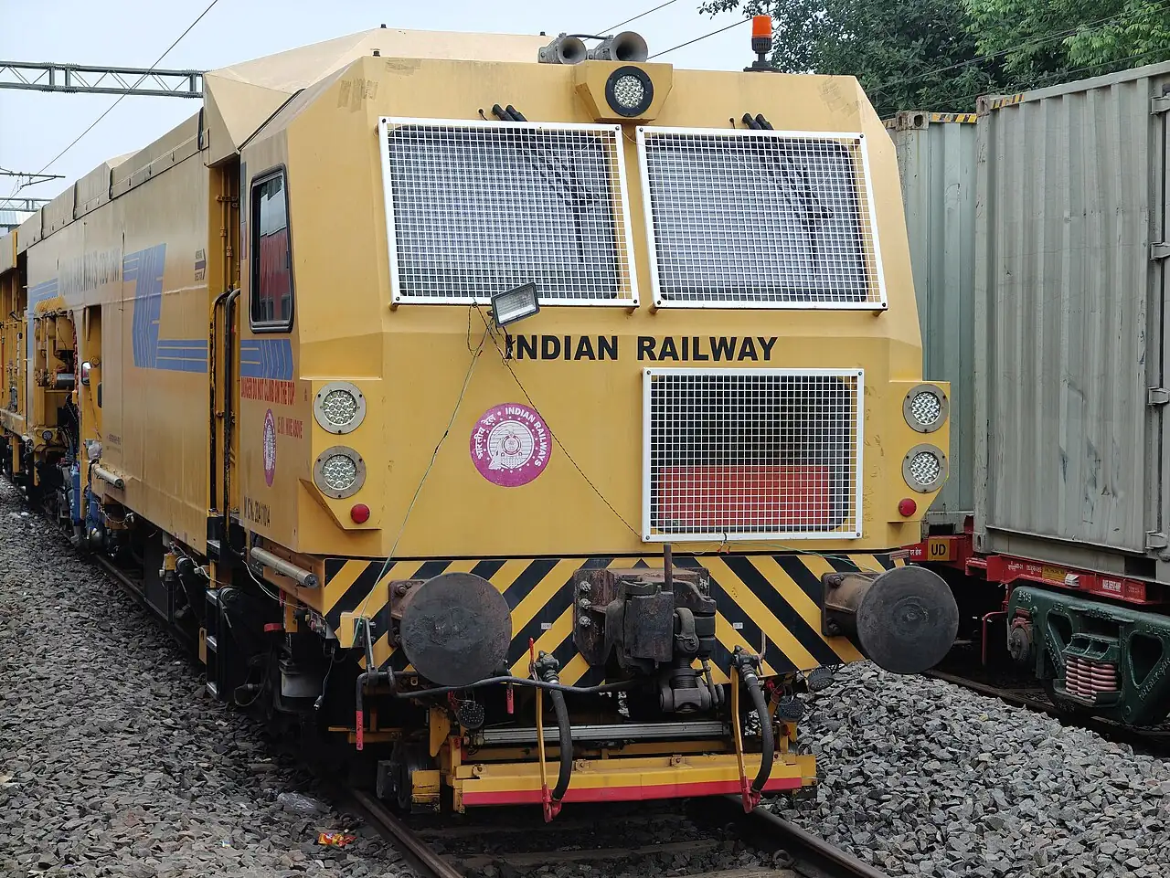 A yellow track-tamping vehicle stands on railway tracks.