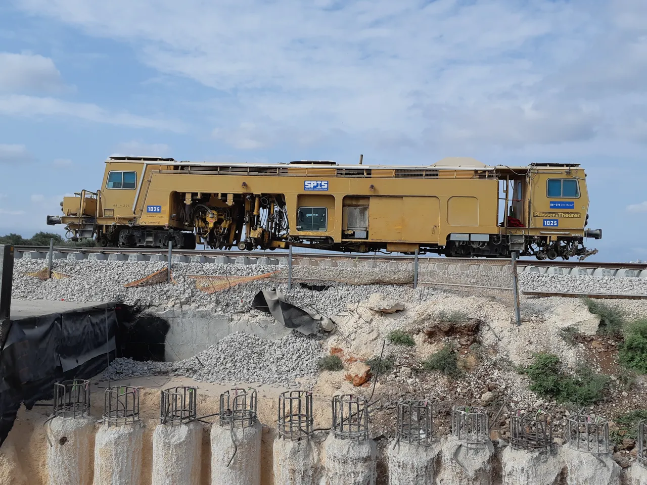 A long yellow track machine has many small wheels and equipment beneath its middle.