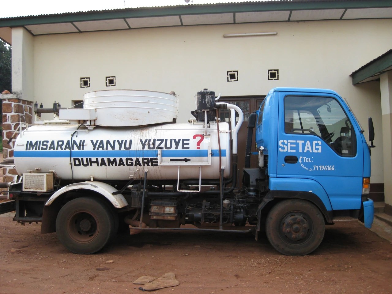 A blue and white vacuum truck shows its round tank, pipes, and cab from the side.