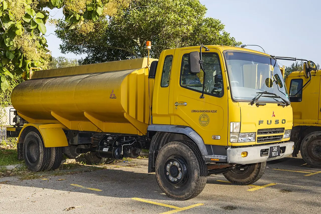 A yellow water truck has a rounded tank behind its cab.