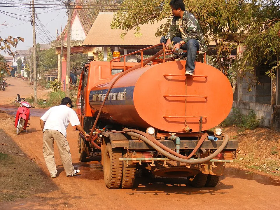 An orange water tanker has thick hoses looped across its back.
